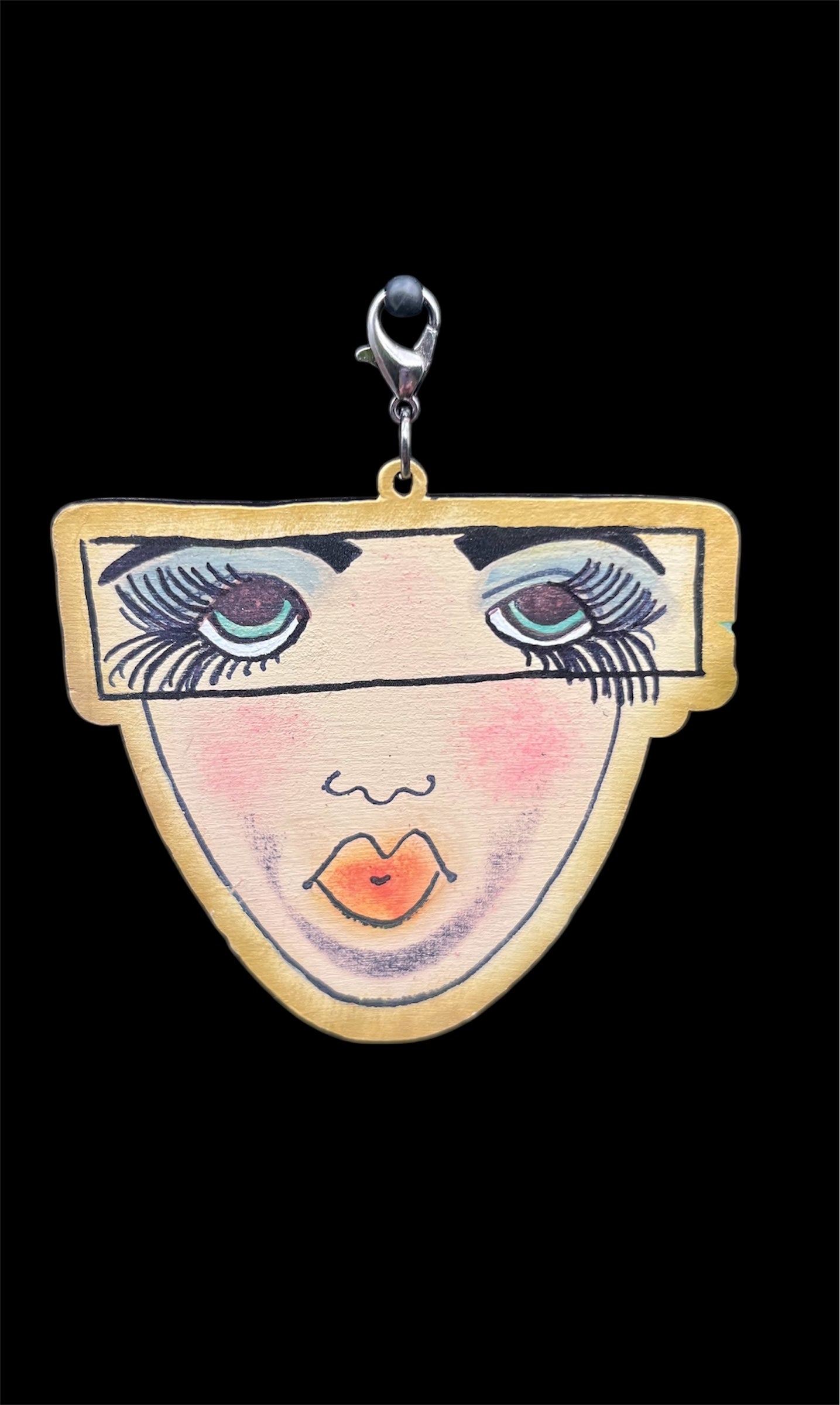 Close-up of a hand-painted wooden face charm with expressive eyes and pink-orange lips, designed for junk journaling and mixed media crafts