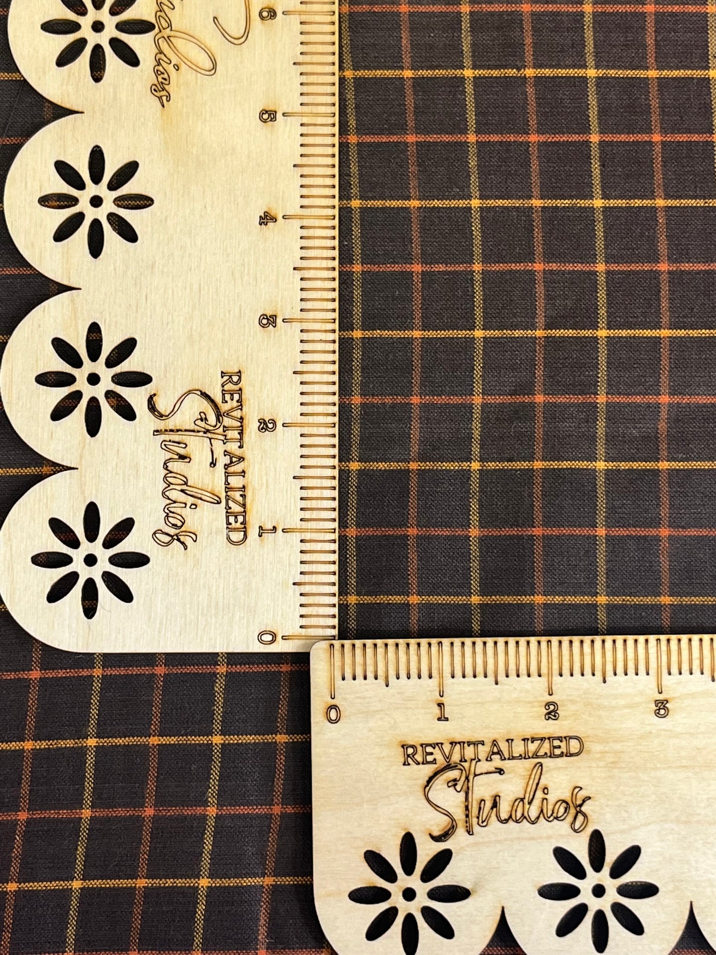 A close-up of a Homespun Fabric fat quarter featuring a large black, gold, and orange checkered pattern, with the brand Andover Fabrics visible. A tape measure is also shown with markings on the fabric.