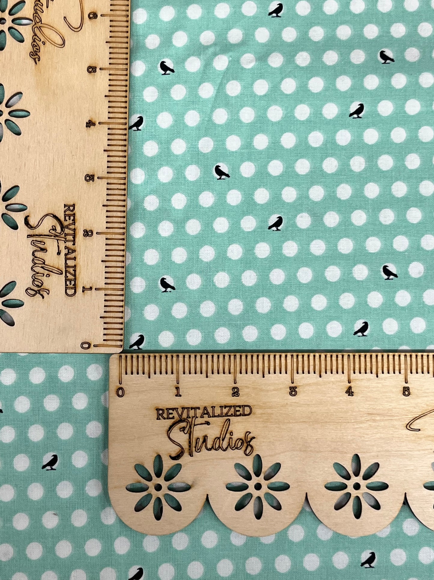 A fat quarter of fabric with a print of black crows on white polka dots against a minty-colored background, with the brand Riley Blake Designs inscribed on the side.