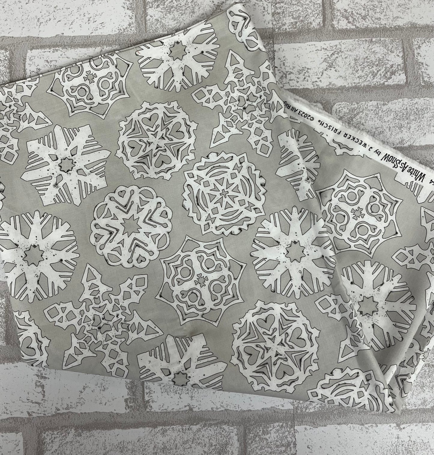 Close-up of Riley Blake White as Snow fat quarter, gray fabric with delicate white snowflakes, perfect for quilting and holiday crafts.