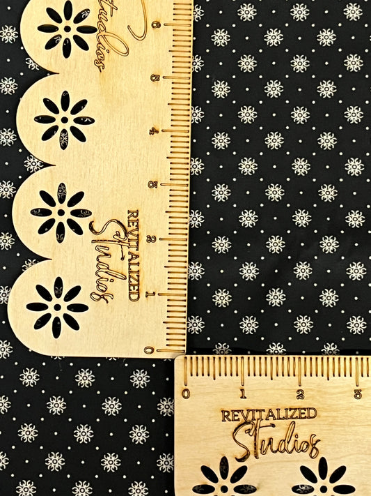Black reproduction fabric with cream floral starburst print by Marshall Dry Goods, shown with ruler for scale.