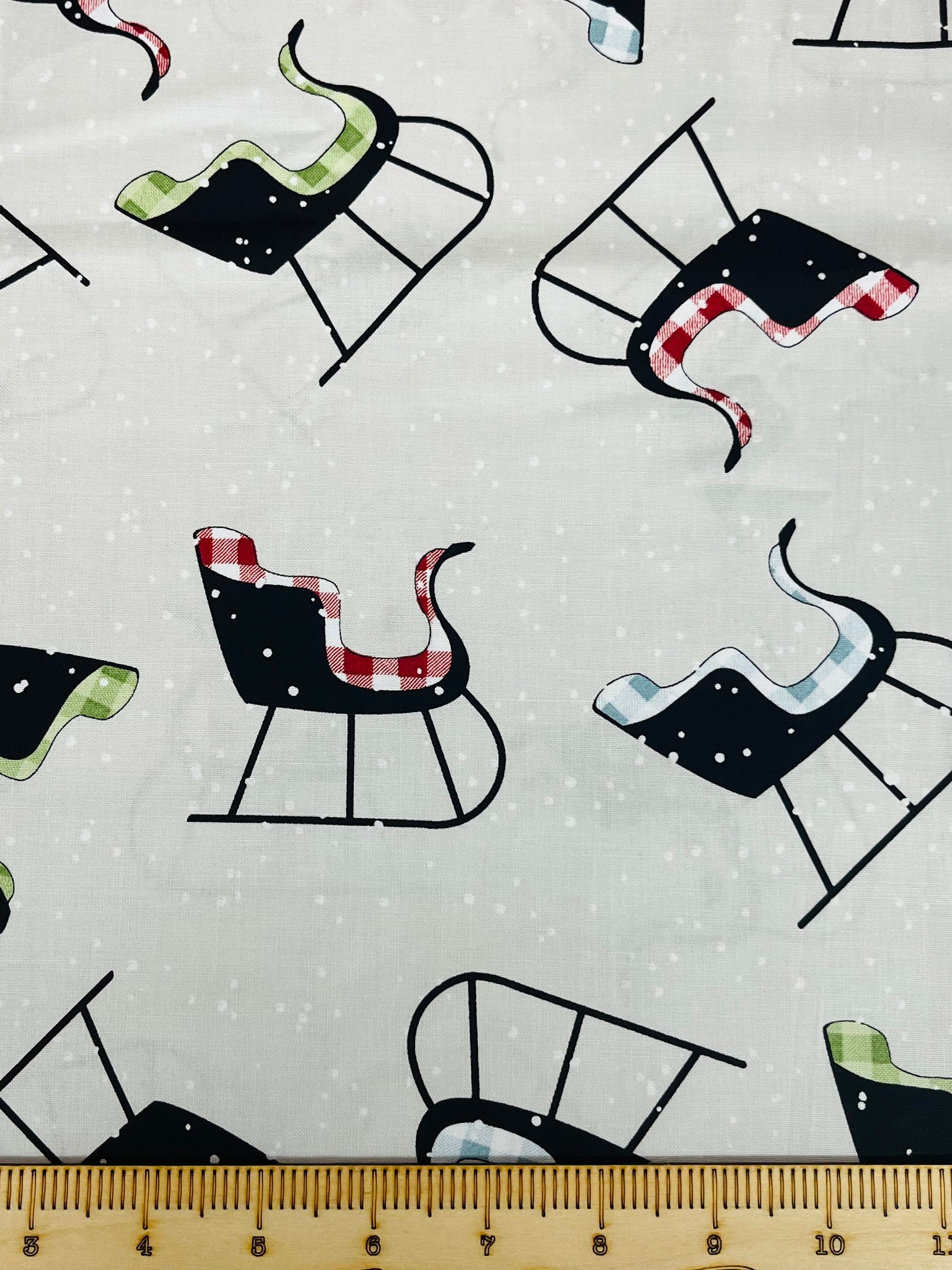 Close-up of Riley Blake Designs White as Snow fabric with whimsical sleighs tossed on a gray background, 100% cotton fat quarter.