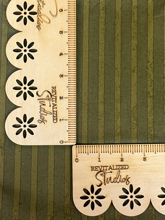 A fabric fat quarter with green stripes and a floral design on it, displayed next to a wooden measuring tape with markings.