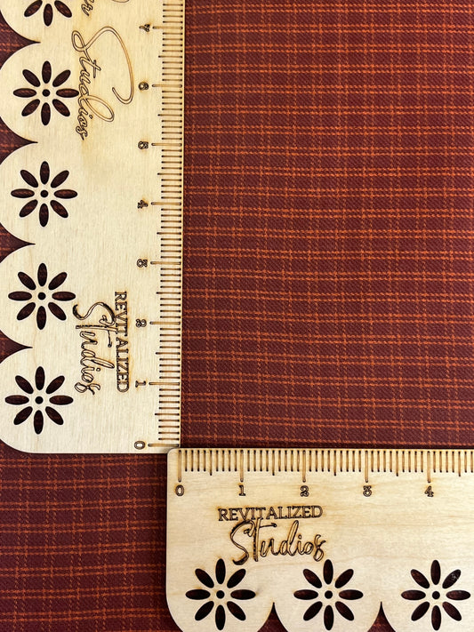 A fabric homespun fat quarter with a brick and orange design, featuring floral patterns on the edges and a ruler with the brand name 'Revitalized Studios' marked on it.
