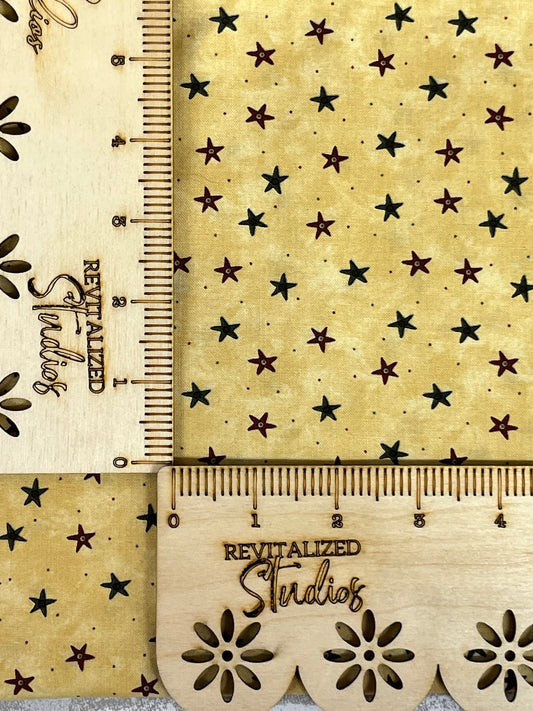 A fabric fat quarter with a gold background and stars of various sizes, as well as a ruler and a brand tag showing the text 'Revitalized Studios'.