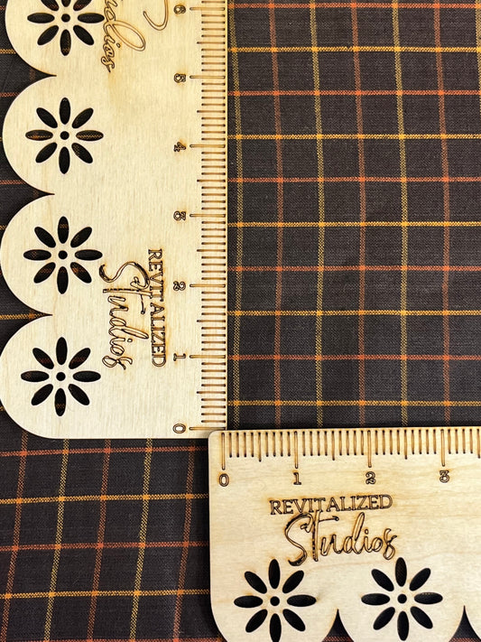 A close-up of a Homespun Fabric fat quarter featuring a large black, gold, and orange checkered pattern, with the brand Andover Fabrics visible. A tape measure is also shown with markings on the fabric.