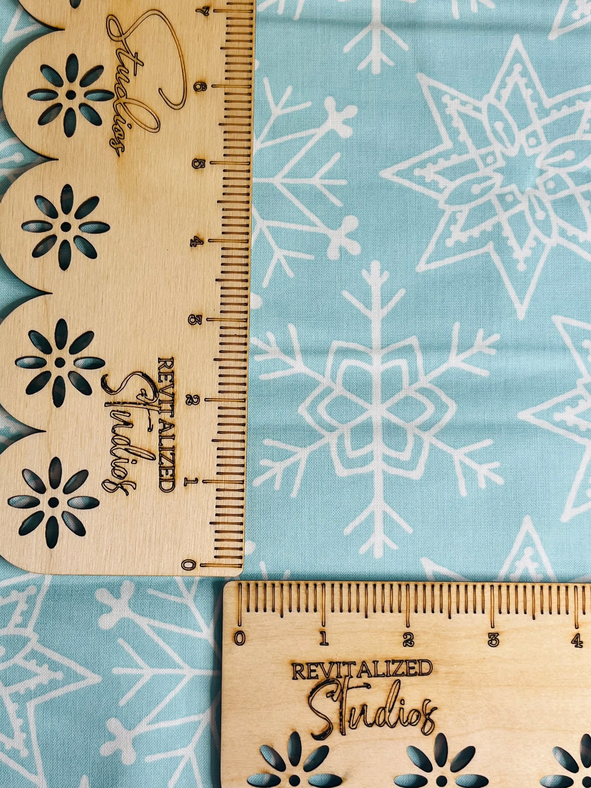 A blue fabric with white snowflake patterns and a wooden ruler with floral designs lying on top of it.