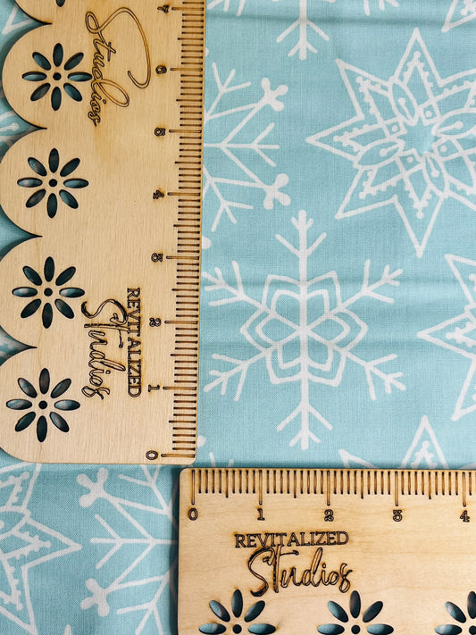 A blue fabric with white snowflake patterns and a wooden ruler with floral designs lying on top of it.