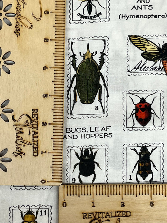A fabric with a series of black and white bug-themed stamps positioned next to a ruler for scale, from the Riley Blake Designs collection.