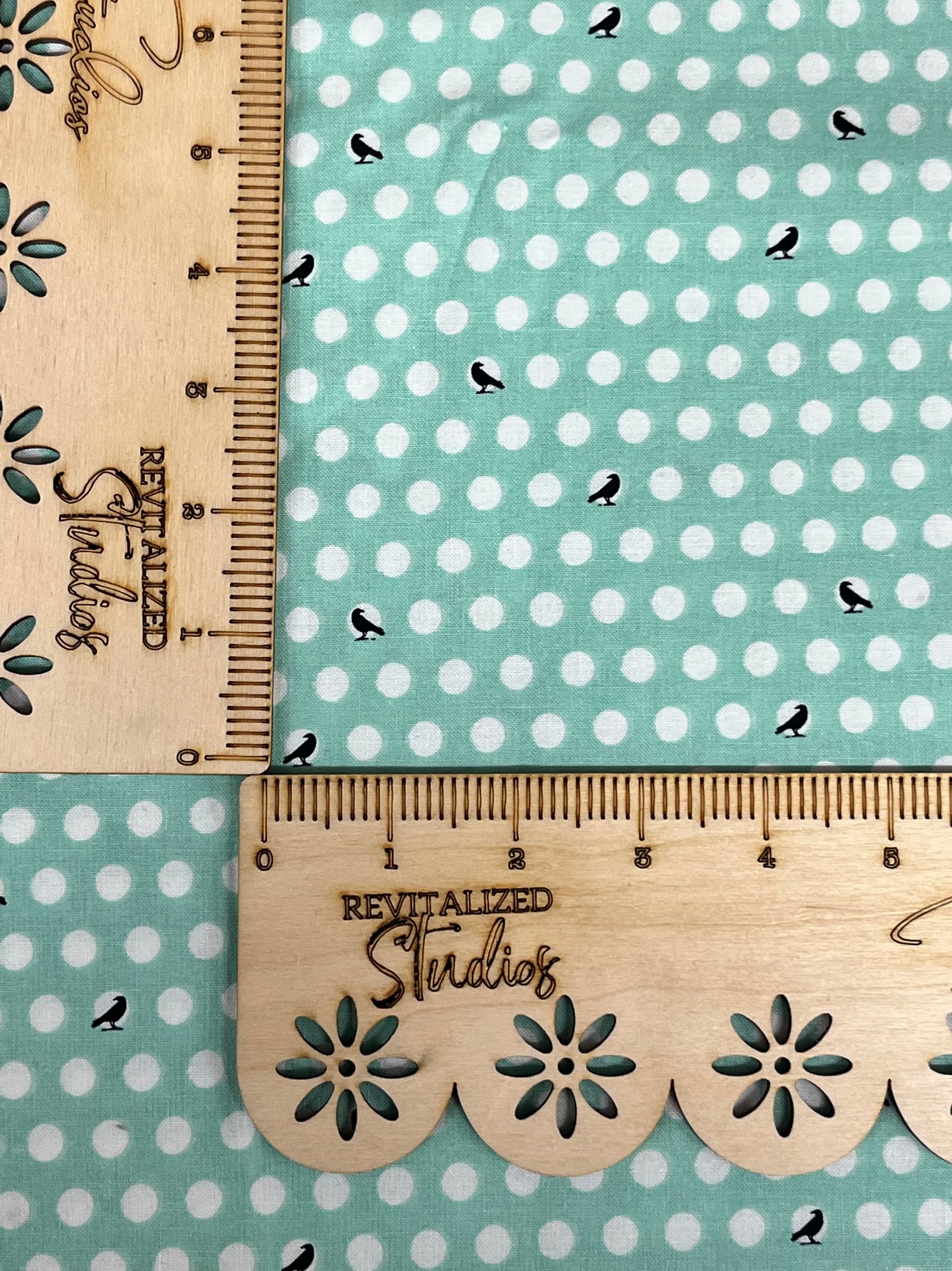A fat quarter of fabric with a print of black crows on white polka dots against a minty-colored background, with the brand Riley Blake Designs inscribed on the side.