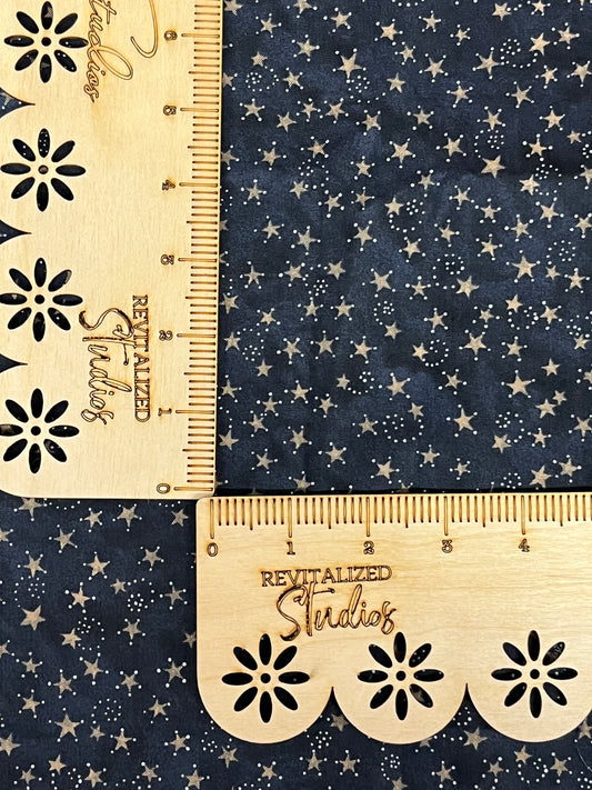 A fat quarter of blue cotton fabric with a pattern of constellations of white stars and dark blue backgrounds, measured with a wooden ruler.