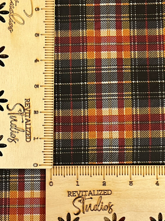 A fat quarter of fabric from the John Wayne Courage Collection with a fall and Halloween plaid pattern. The fabric is primarily black, orange, red, yellow, and white, and the image includes a ruler for scale.