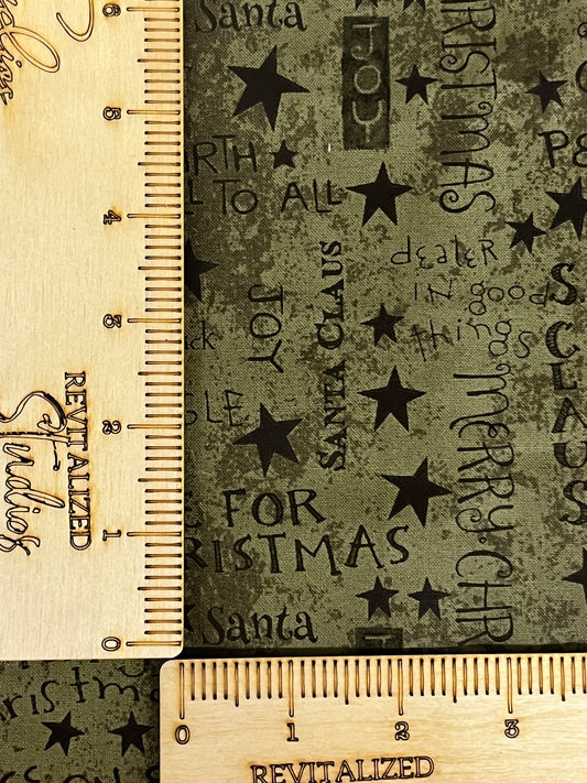 A fat quarter of green fabric with Christmas sentiments and stars pattern, measured with a yellow tape measure.