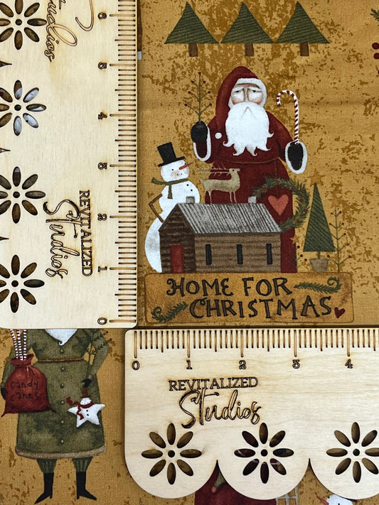 A fabric fat quarter featuring a rustic design with an illustration of Santa Claus, a reindeer, and a Christmas tree on a mustard/brown backdrop. The text on the fabric reads 'Home for Christmas' and 'Revitalized Studios'.