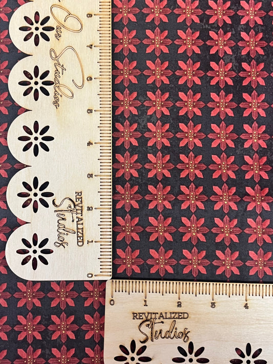 A fabric fat quarter with a Christmas-themed pattern featuring poinsettias on a black background, alongside a ruler with measurements.
