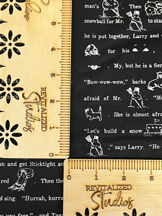 Fabric from the White As Snow Collection with fun words printed in a black background, and a wooden ruler with Christmas themed illustrations and text.