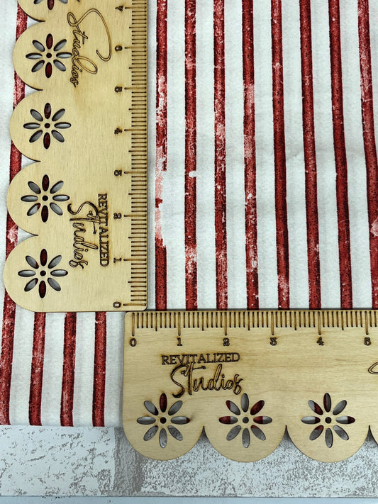 Fabric with red and white striped pattern and a gold-colored scale ruler with floral designs and the text 'Streaks'.