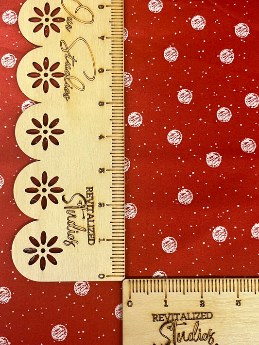 A fat quarter piece of fabric with a white snowball pattern on a red background, alongside a wooden ruler with markings.