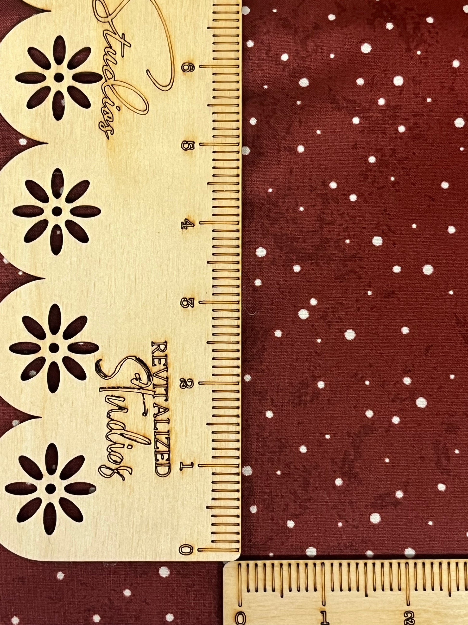 A fabric from the Kringle Collection by Teresa Kogut, featuring white dots on a red background, displayed next to a ruler for scale.