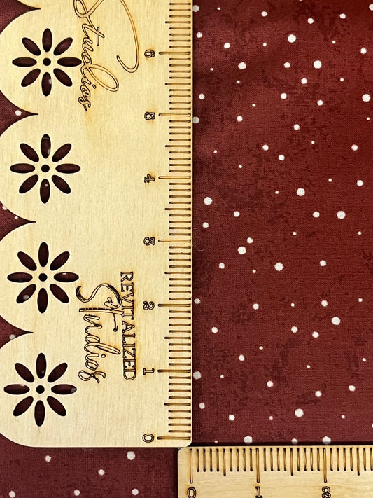 A fabric from the Kringle Collection by Teresa Kogut, featuring white dots on a red background, displayed next to a ruler for scale.